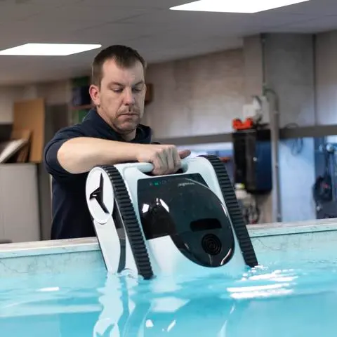 Ein Techniker hebt einen Poolroboter aus dem Wasser